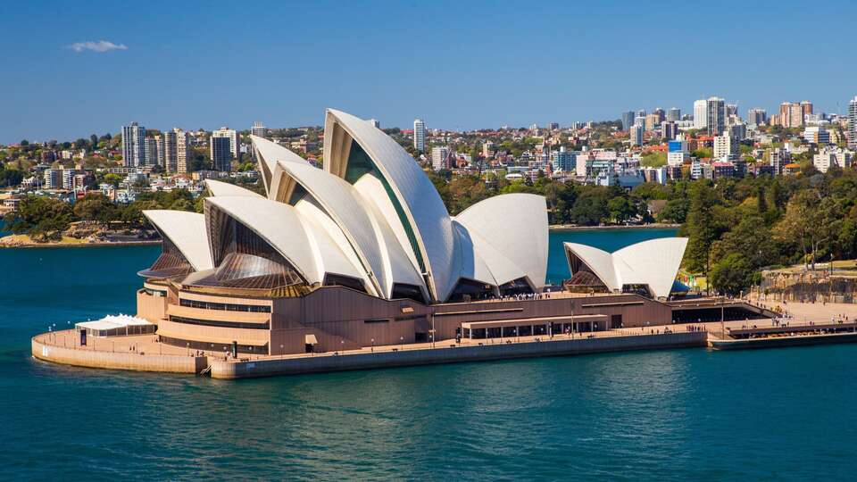 The Sydney Opera House surrounded by blue water under a clear sky.