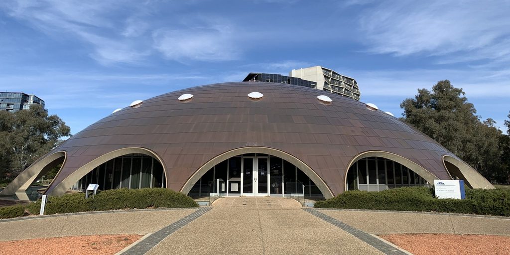 A large, dome-shaped building with arched entrances surrounded by trees.