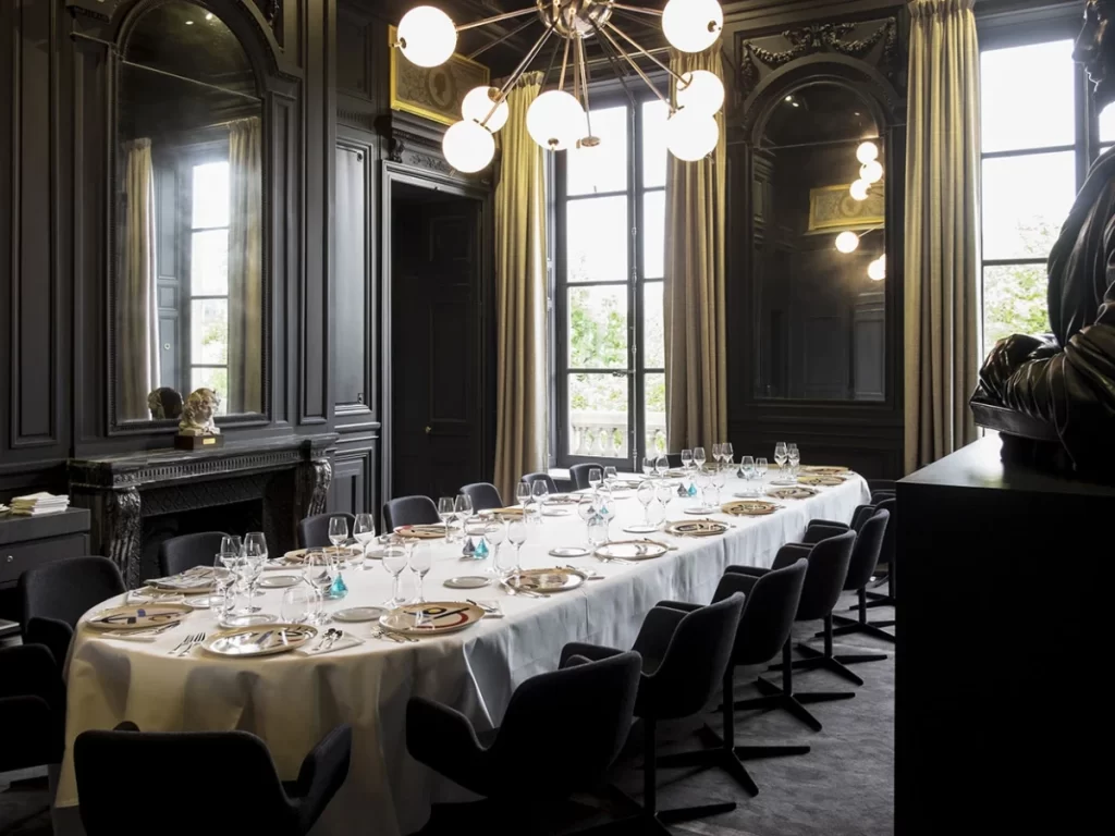 Formal private dining room featuring a long white table, dark walls, and a modern chandelier.