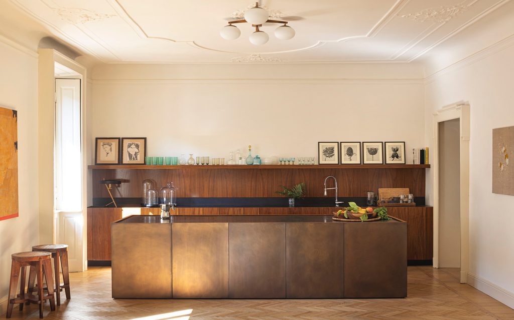 Spacious modern kitchen with a large metallic bronze island, wood-paneled back counter, and classic herringbone parquet flooring. top interior design firms in milan